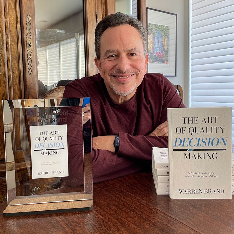 Author Warren Brand displays copies of his book The Art of Quality Decision Making